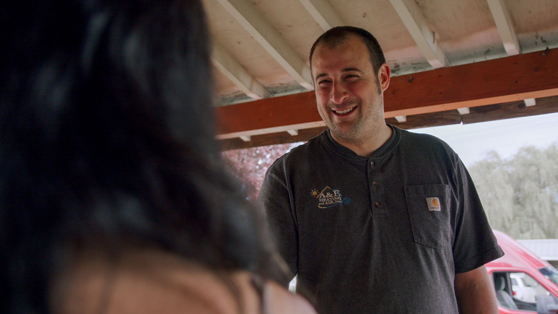 A&E tech talking to a woman in front of a door on the porch of her house, a smile on his face, implying a job-well-done.