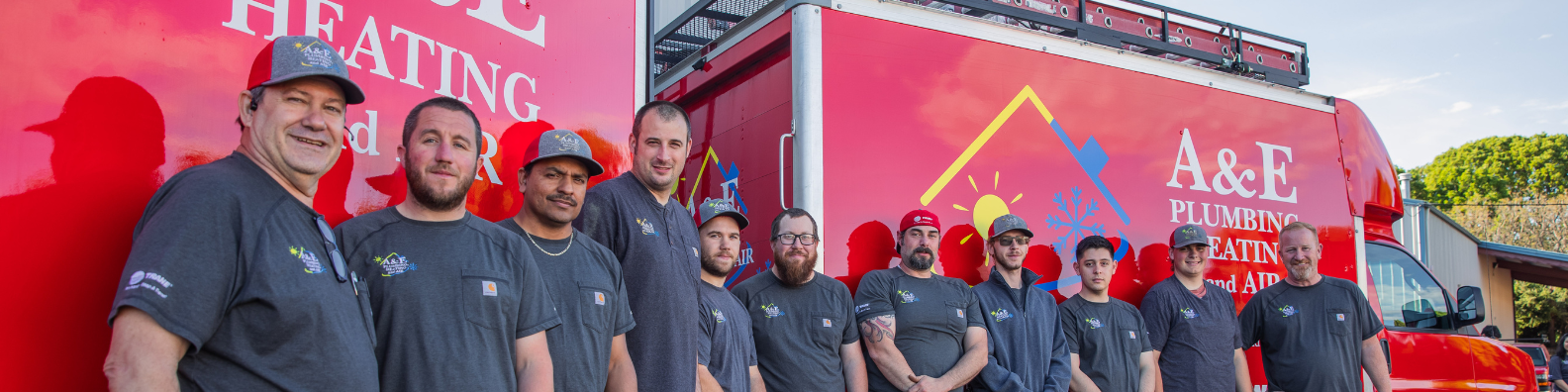 A group shot of A&E Plumbing, Heating and Air technicians in front of bright red company vans.