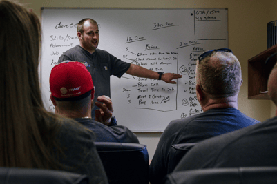 An A&E tech stands before a room of other HVAC techs, teaching about HVAC best practices within A&E.