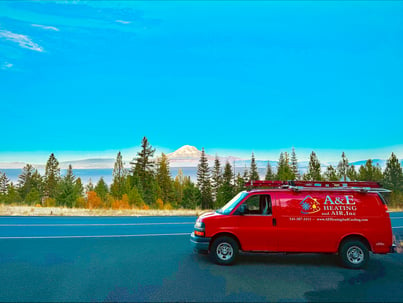 An A&amp;E red company van sits on the shoulder of a highway, Mount Hood in the background on a clear, sunny day.