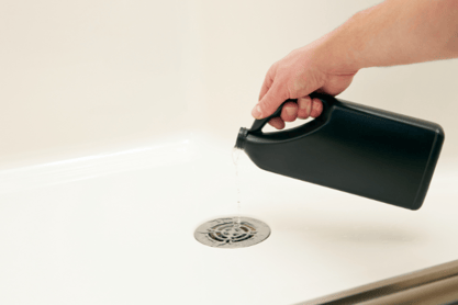 A hand pours acidic drain cleaner down a residential drain.