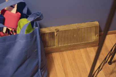 A bag sits in front of a floor HVAC vent, serving as an example of what NOT to do.