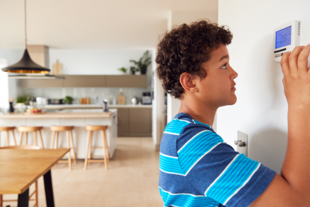 A boy adjusts the temperature of a wall-mounted Trane smart thermostat.