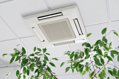 A vent connected to a central air HVAC system is placed in a ceiling with green shrubbery reaching towards it.