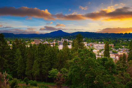 An outdoor shot of the city of Gresham behind trees, buildings barely visible past the branches.