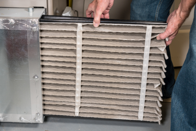 A man holds up a dirty air filter straight from the HVAC system.