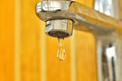 A close-up shot of water dripping from a standard home faucet.