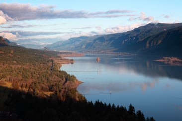 I-84 winds along the Columbia River in this aerial shot, clouds and hills in the distance.