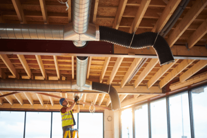 An HVAC technician works to install ductwork in a new home construction frame.