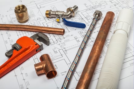 Plumbing components, including copper and PEX pipes, lay on a home blueprint.