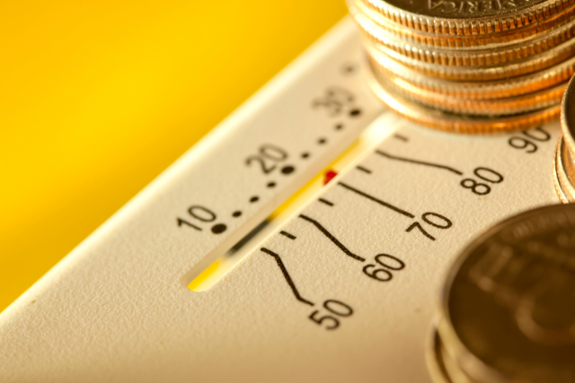 A pile of coins sits on an HVAC home thermostat, indicating that it's causing high utility bills.