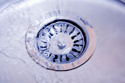 A drain screen sits in a residential drain hole with water running through it.