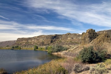 Columns of basalt rock sit next to a pond, the scene surrounded by dry Washington high desert land.