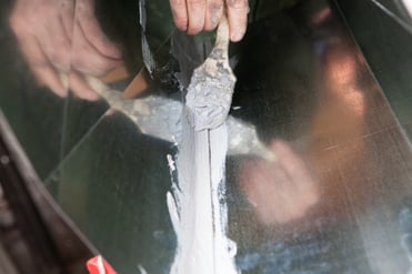 A person applies mastic duct sealing on a residential HVAC duct with a paintbrush. 