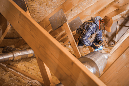 An HVAC tech works on repairing a home's ductwork in the attic.