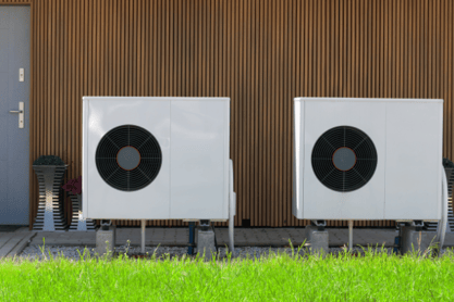 Two outdoor heat pumps sit side-by-side next to a residential house.