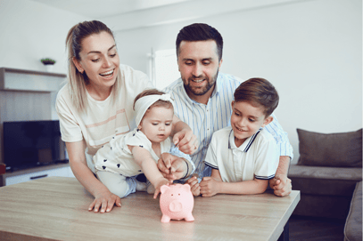 A family of 4 watches with smiles as the youngest member put a coin in their pink piggy bank, implying great savings and happiness.