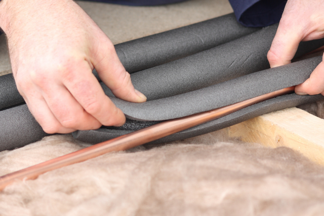 A set of hands places foam pipe insulation over a copper pipe.