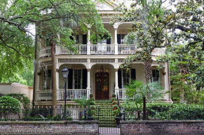 White historic home surrounded by decorative black fencing and green foliage.