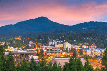 Gresham City in the summer as the sun sets: vibrant pink paints the horizon above the hills with the city lights below.