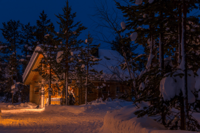 House with indoor lights on at night in a snowy setting.