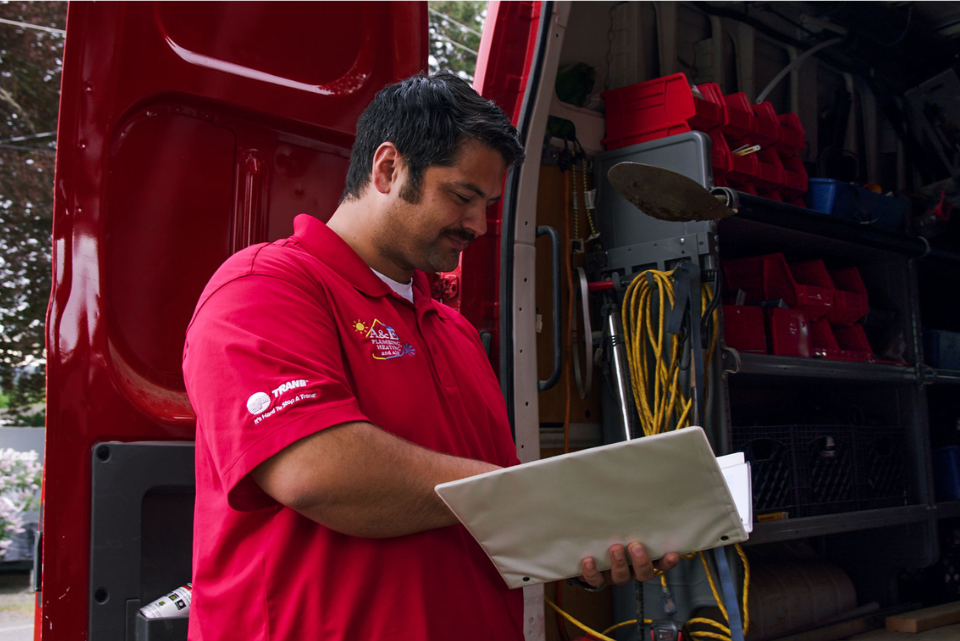 An A&E tech looks down at the paperwork in his white binder, a smile on his face to show he's happy with a job well done.