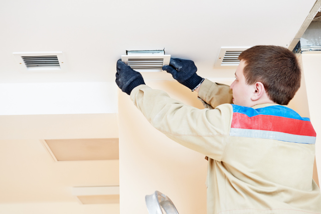 An HVAC tech reaches up to change out the ventilation grate on a homeowner's ceiling. 