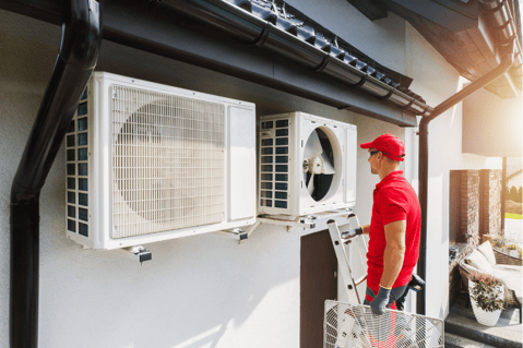 An HVAC technician stands on a ladder to work on an outdoor HVAC unit.