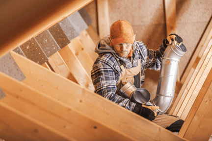 An HVAC tech works to install new ductwork in a residential attic.