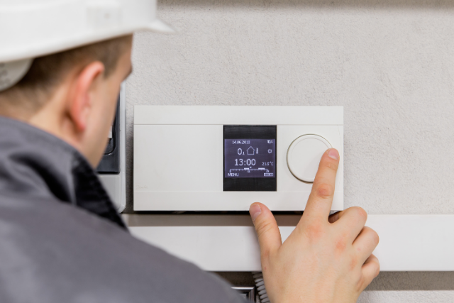 An HVAC tech works on a wall-mounted Trane smart thermostat.