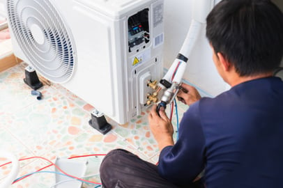 An HVAC tech works to install a new HVAC unit on a speckled residential floor.