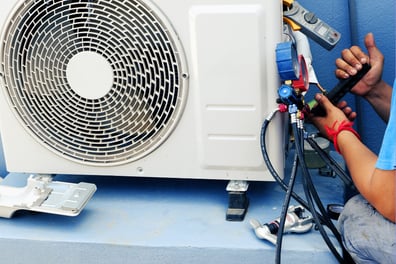 A man sits besides an HVAC unit, tools in hand to improve efficiency. 