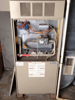 An older furnace with its cover panel removed to show surface-level circuitry and mechanics.