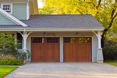 A two-car attached garage sits surrounded by lush, green foliage.