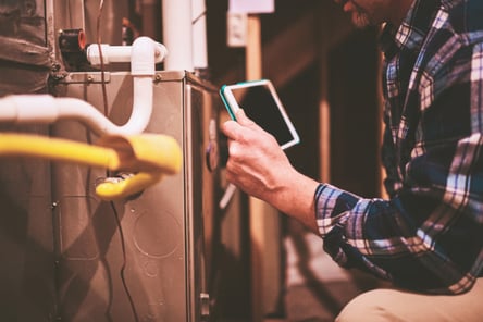 A man checks the health of an HVAC home furnace with a screen.