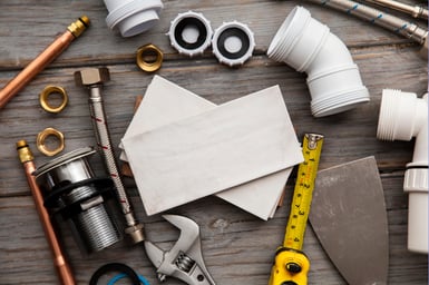 Piping components sit on a wood backdrop, implying an active plumbing job by an A&E plumber is happening.