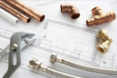 Copper piping and other plumbing tools sits on top of a home's layout, implying a plumber at work.