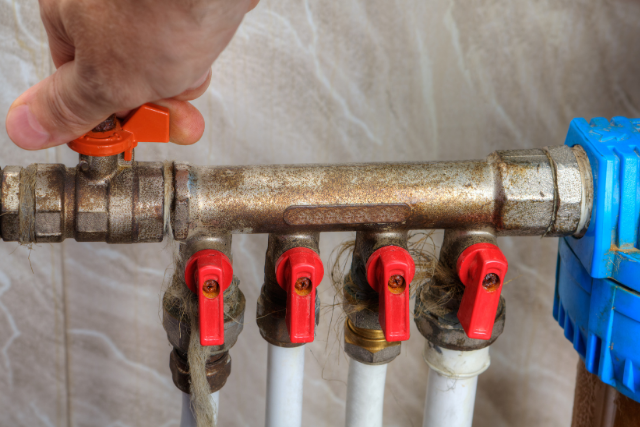 A hand reaches over to turn off the water valve for their home.