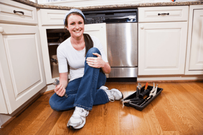 A homeowner sits in front of her sink plumbing, tools in hand to perform simple routine plumbing maintenance.