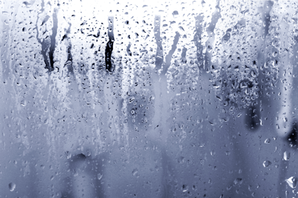 A window with an excess amount of humidity accumulated over a grey background. 