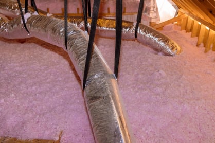 Ductwork in an attic surrounded by insulation.