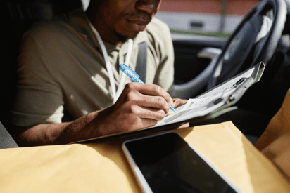 A man sits in his car with a clipboard in hand, presumably filling out the paperwork to get an HVAC written estimate for his client.