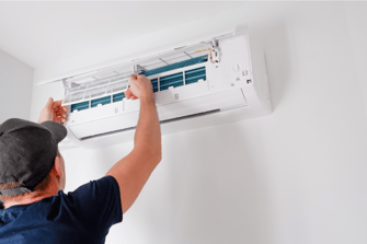 A man reaches up to work on an indoor mini split, inspecting the filter.