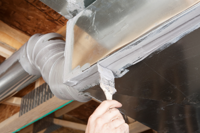 A person applies mastic duct sealing to a residential duct with a paintbrush.