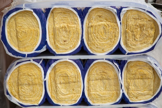 A stack of 4 rolls of yellow mineral wool insulation lay on one another.