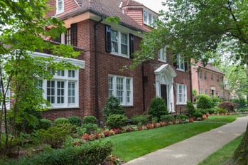 An older home with outdated ductwork sits next to the sidewalk.