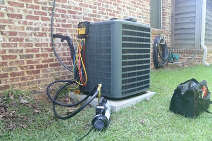 An older outdoor HVAC unit sits on a concrete pad with diagnostic tools connected to it, checking the system performance.