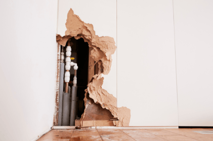 A section of residential wall is removed to expose older pipes underneath.