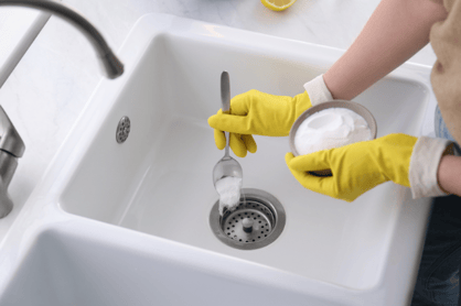 A hand scoops oxidizing drain cleaner into a residential kitchen sink.