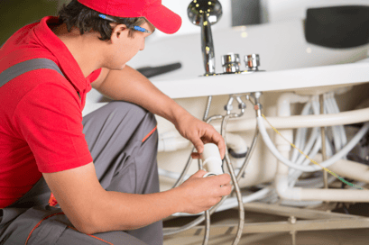 A plumber works to replace pipes under a residential bathtub.